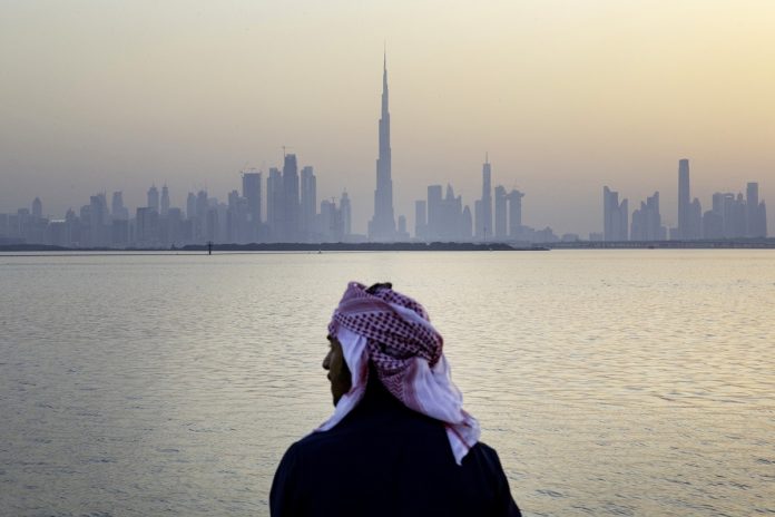 An Emirati man looks out from the Dubai Creek Habour Development towards the Burj Khalifa tower, center, and other skyscrapers in Dubai, United Arab Emirates, UAE
